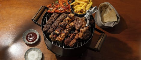 A grill with various meats and sides including fries, flatbread, and condiments.