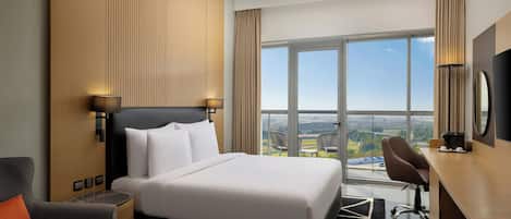 A hotel room with a bed, a desk, a chair, and a large window offering a city view.