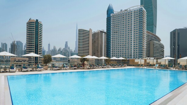 A swimming pool with lounge chairs and umbrellas, surrounded by high-rise buildings.