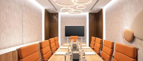 Un salón de conferencias con una larga mesa, sillas naranja, una pantalla grande e iluminación moderna.