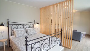 A neatly arranged bedroom with a bed, bedside lamps, a small table, and a grey sofa.