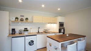 A compact kitchen with a washing machine, a microwave, a coffee maker, and a wooden table with chairs.