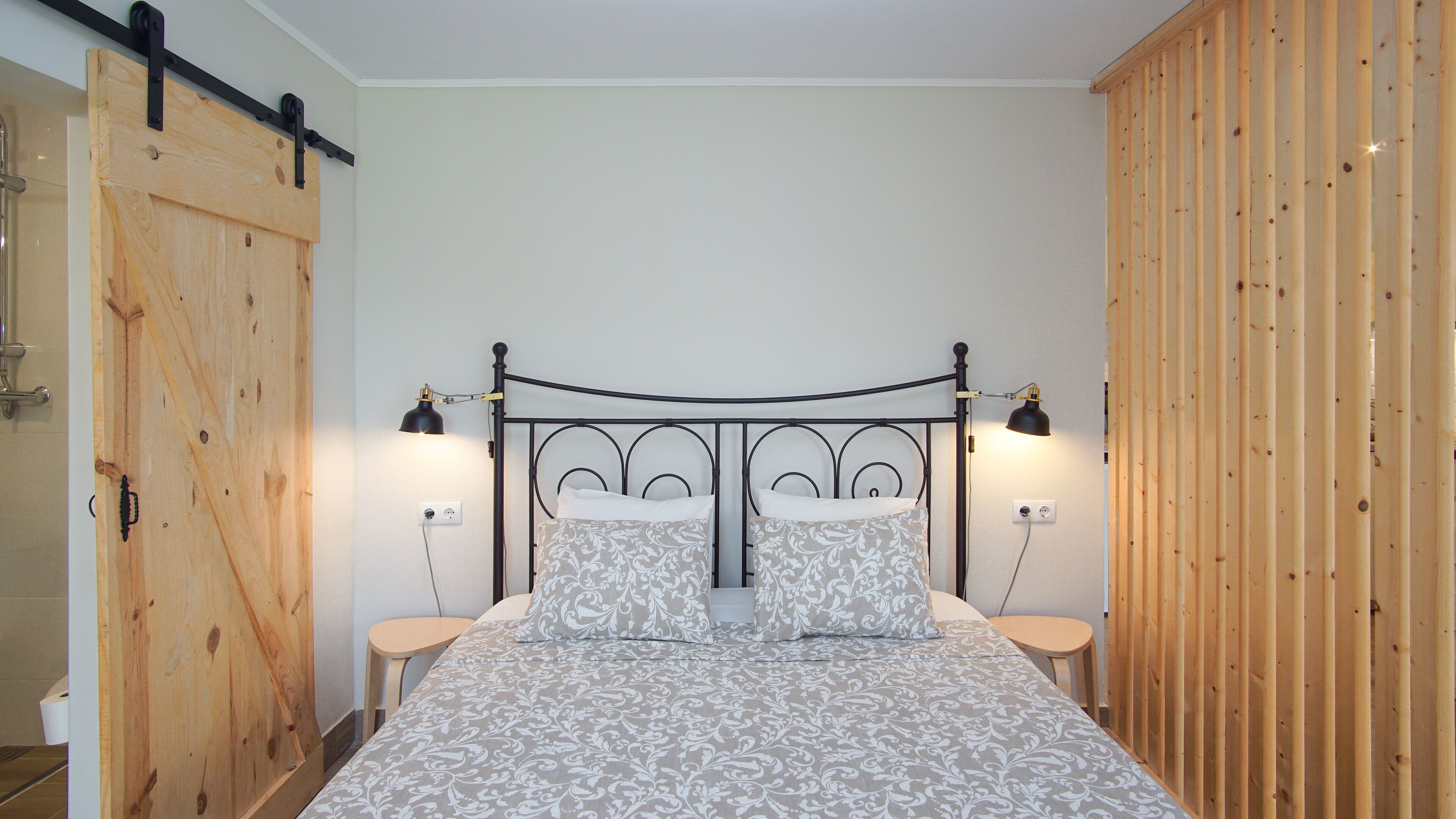 Un dormitorio con estructura metálica para la cama, dos mesitas de noche, un armario de madera y una pared divisoria de madera.