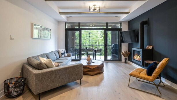 Una sala de estar moderna con un sofá, una mesa de centro y un sillón. Hay una chimenea y un televisor en la pared.