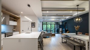 Una cocina moderna con una isla central, taburetes de bar y una zona de comedor con una mesa larga y bancos.