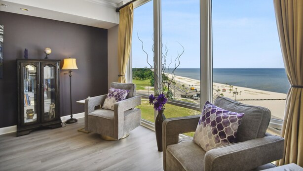 Ein Zimmer mit zwei grauen Sofas, einer Stehlampe, einem Globus und Blick auf den Strand.
