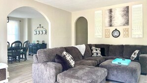 A living room with a grey sectional sofa, a dining area with a table and chairs, and a kitchen in the background. - New Remodel in St. Charles - Sleeps 10! New patio! Large Fenced-in backyard! (Saint Charles)