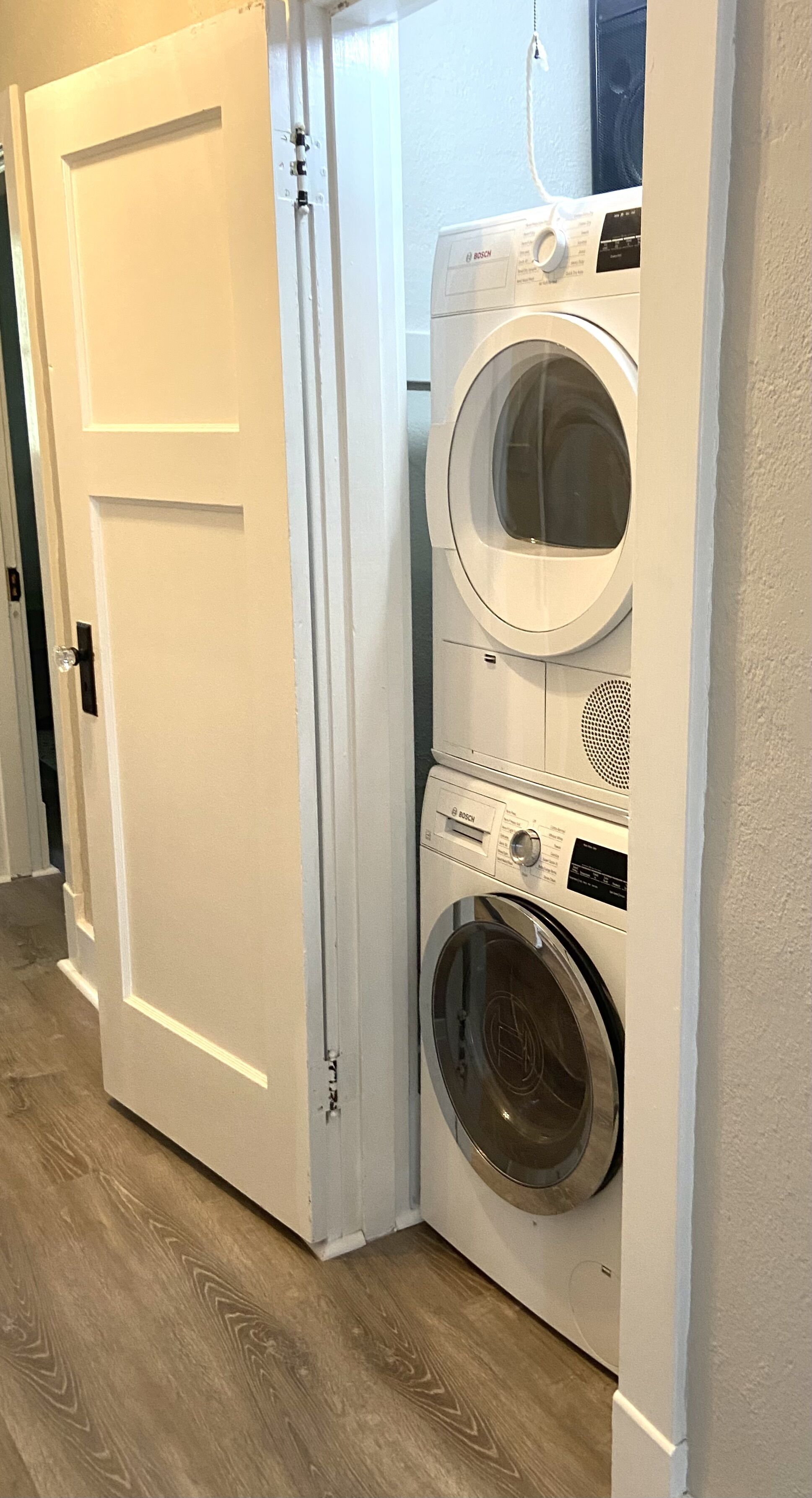 A laundry room with two stacked front-loading washing machines and a white door.