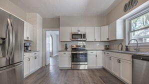 A modern kitchen with stainless steel appliances, white cabinetry, and a wooden floor. - New Remodel in St. Charles - Sleeps 10! New patio! Large Fenced-in backyard! (Saint Charles)