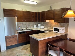 A kitchen with wooden cabinets, a built-in dishwasher, a microwave, a coffee maker, and a dining table with chairs. - "Yves am See" Vacation Apartment in the Gaienhofen/Horn Nature Reserve (Gaienhofen)