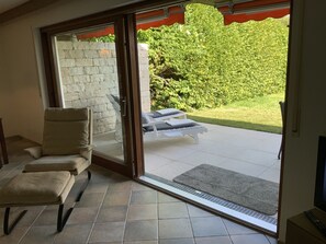 Ein Zimmer mit einer Schiebetür zu einer Terrasse, auf der eine weiße Lounge-Liege und ein kleiner Tisch stehen.