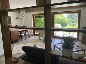 Ein modernes Wohnzimmer mit einer Couch, einem Couchtisch und einem Essbereich mit Stühlen und Tisch. Ein großes Fenster bietet einen Ausblick ins Freie.