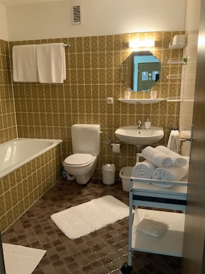 Un baño con bañera, inodoro, lavamanos y un toallero con toallas.