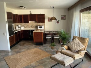 A modern kitchen with dark wood cabinets, a central island, and a dining area with a sofa and a plant. - "Yves am See" Vacation Apartment in the Gaienhofen/Horn Nature Reserve (Gaienhofen)