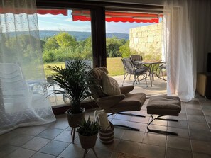 A room with a view of a green landscape, a sofa, a table, and chairs. - "Yves am See" Vacation Apartment in the Gaienhofen/Horn Nature Reserve (Gaienhofen)