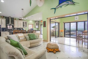 A spacious living area with a sofa, a turtle-shaped ottoman, and a view of the ocean through large sliding doors.