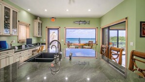 Una cocina con vista al océano, un comedor con mesa y sillas, y una gran decoración de pescado en la pared.