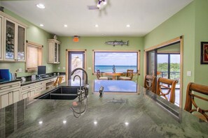 A kitchen with a view of the ocean, a dining area with a table and chairs, and a large fish decoration on the wall.