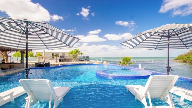 Una piscina con dos sillas reclinables blancas y sombrillas a rayas, un jacuzzi y vistas al océano.