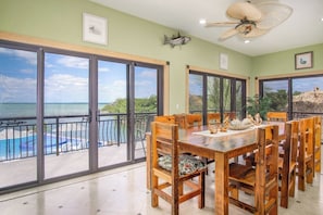 A dining area with a view of the ocean, a ceiling fan, and a poolside.