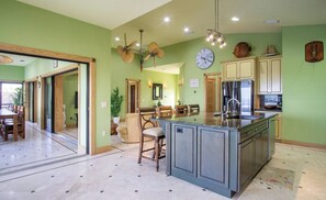 Una cocina con una isla central, un comedor con sillas y un reloj en la pared.
