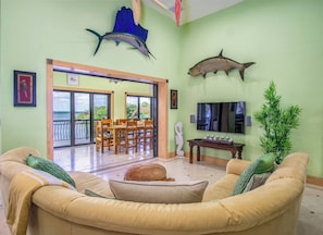 A living room with a sofa, a dining table, chairs, a TV, and two fish mounted on the wall.
