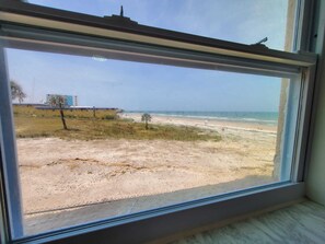 Blick aus dem Fenster auf einen Strand mit einem Gebäude im Hintergrund.