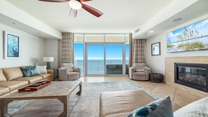 A spacious living room with a large sliding glass door leading to a balcony with a view of the ocean. There is a fireplace, a sofa set, and a coffee table. - Turquoise Place!  New Rental!! (Orange Beach)