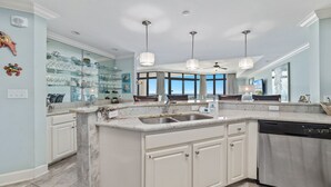 A modern kitchen with a large island, glass shelving, and pendant lighting. - New Rental!! Oasis, Formerly Phoenix West II, Lazy River and Slide!4th FLOOR! (Orange Beach)