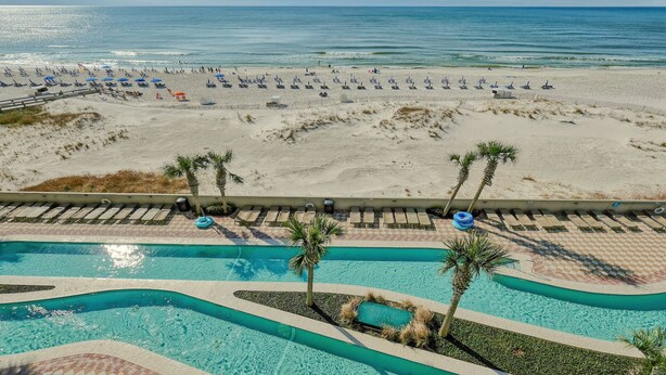 A pool area with palm trees, a beach in the background, and lounge chairs. - New Rental!! Oasis, Formerly Phoenix West II, Lazy River and Slide!4th FLOOR! (Orange Beach)