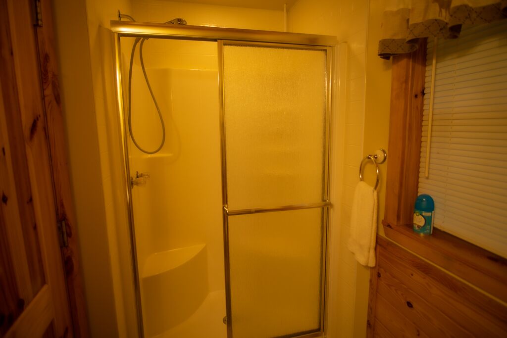 Una ducha con puerta de vidrio, una toalla colgada en la pared y una ventana con persianas.