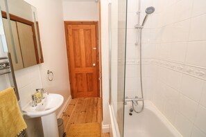 A bathroom with a wooden door, a white sink, and a glass-enclosed shower. - Trevedran Cottage (Penzance)