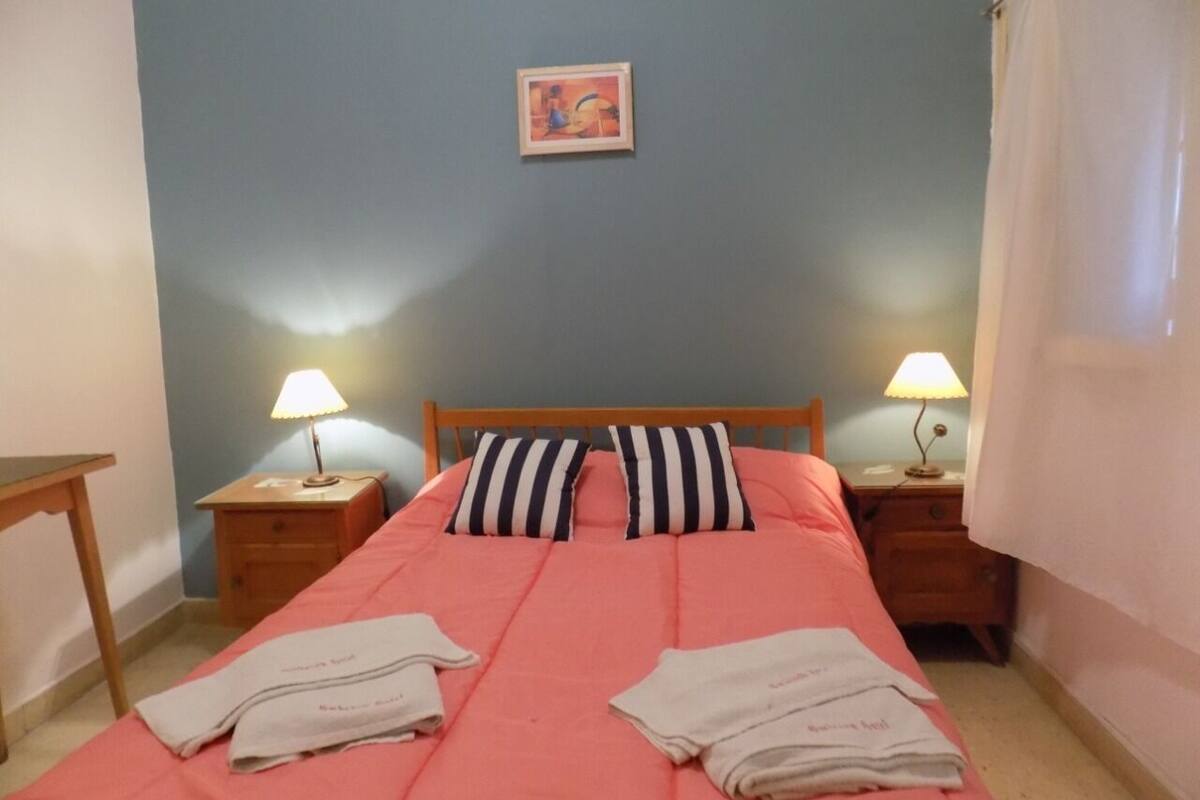 A bedroom with a bed, two bedside tables with lamps, a painting on the wall, and a door.