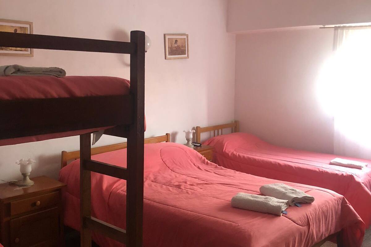 A dormitory room with bunk beds, a nightstand, a lamp, and a window with curtains.