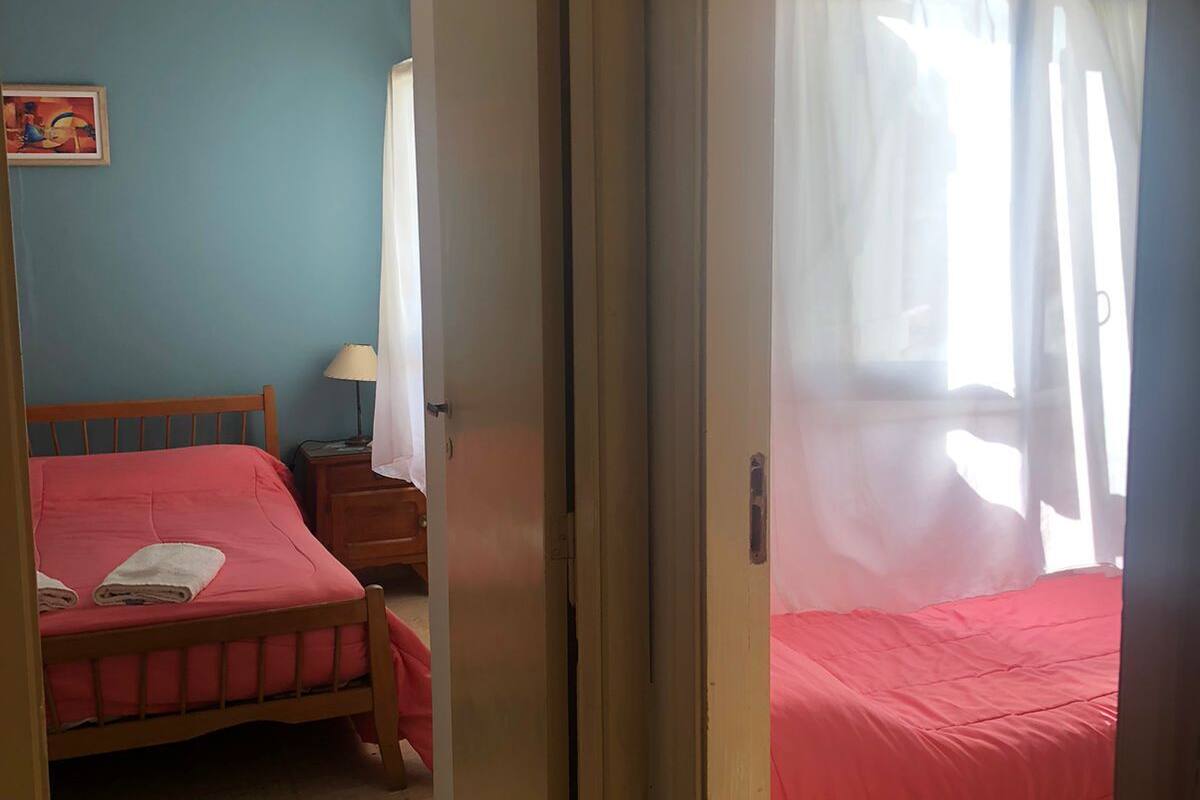 A room with two beds, a wooden headboard, a nightstand, a lamp, and a painting on the wall.