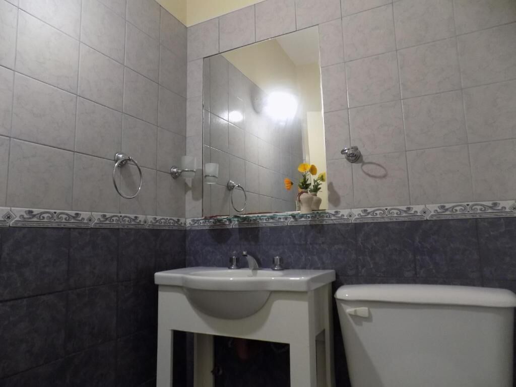 A bathroom with grey tiles, a white sink, a toilet, and a mirror.
