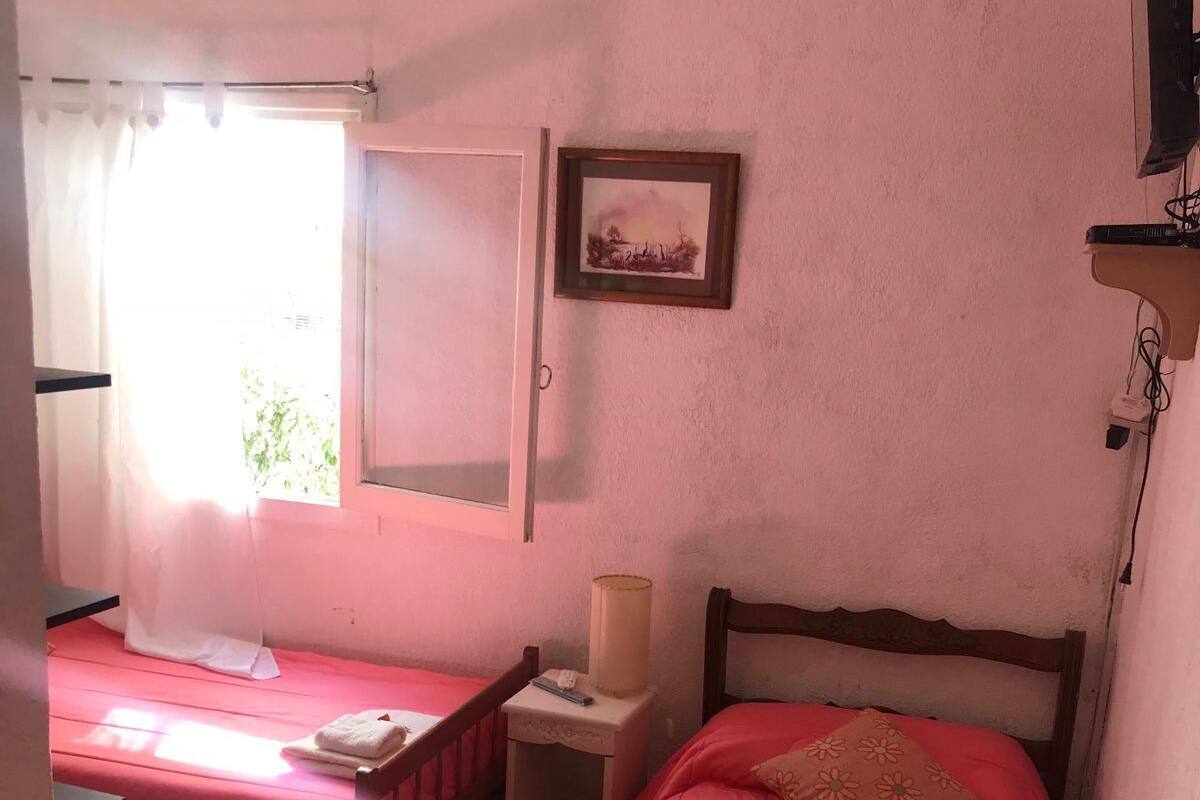 A room with two beds, each with a pink bedspread and a white towel. There is a small bedside table with a lamp and a framed picture on the wall.