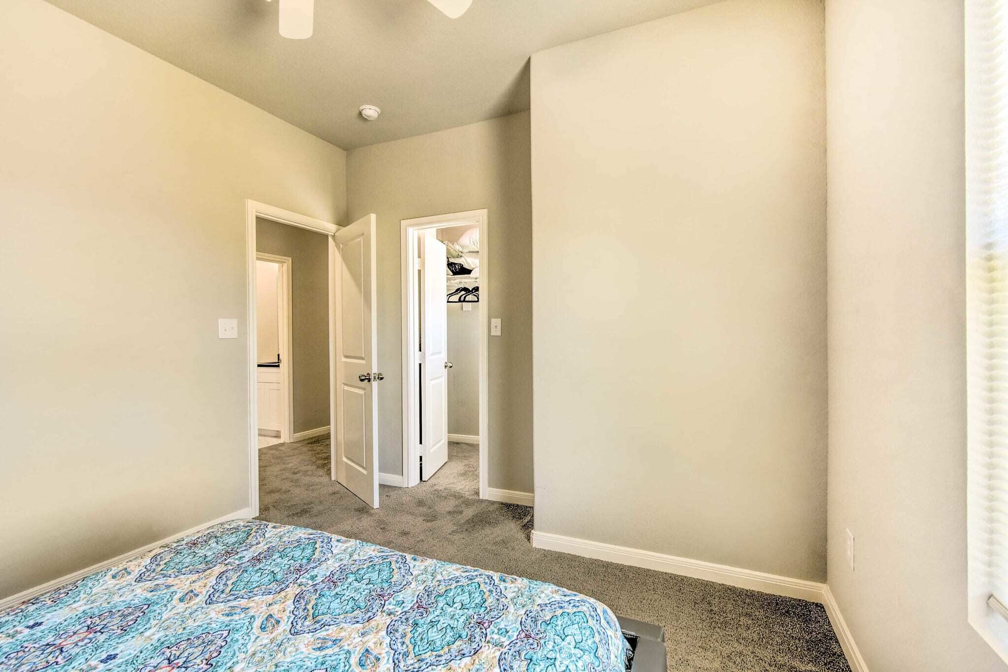 A bedroom with a bed, carpeted floor, and a closet with hanging clothes.
