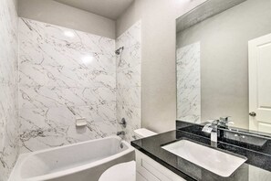 Ein modernes Badezimmer mit einer Duschwand aus Marmor, einer Badewanne, einem Waschbecken und einem großen Spiegel.