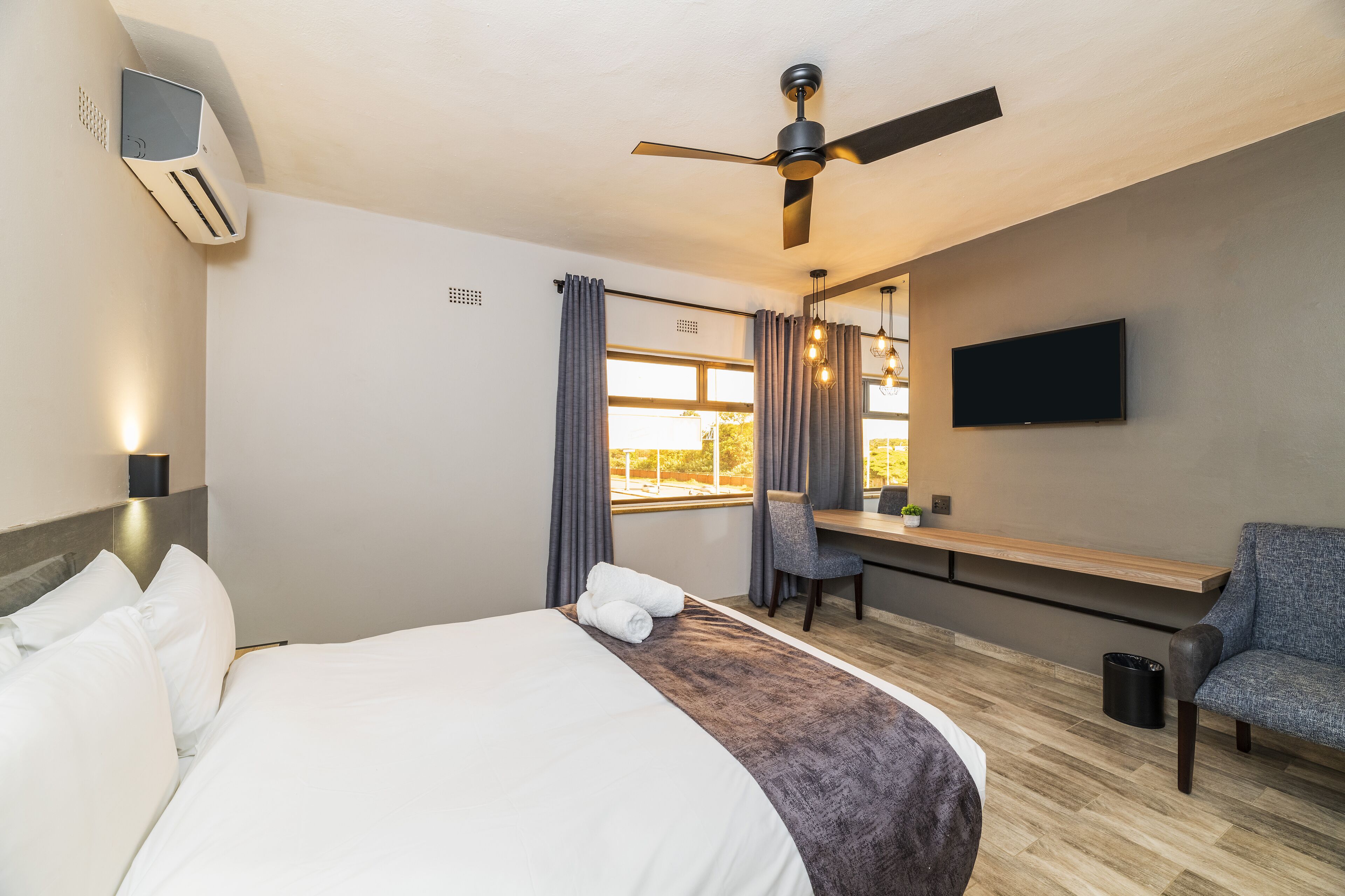 Una habitación de hotel con cama, escritorio, silla, televisión y ventilador de techo.