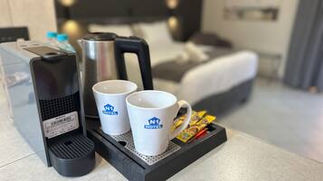 Una cafetera, dos tazas blancas con el logo del hotel y una bandeja con cápsulas de café sobre la encimera de la habitación.