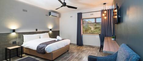 A modern hotel room with a bed, a desk, a chair, a ceiling fan, and a window with curtains.