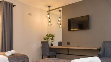 Una habitación de hotel moderna con cama, dos sillones, un escritorio, televisor de pantalla plana y lámparas colgantes.