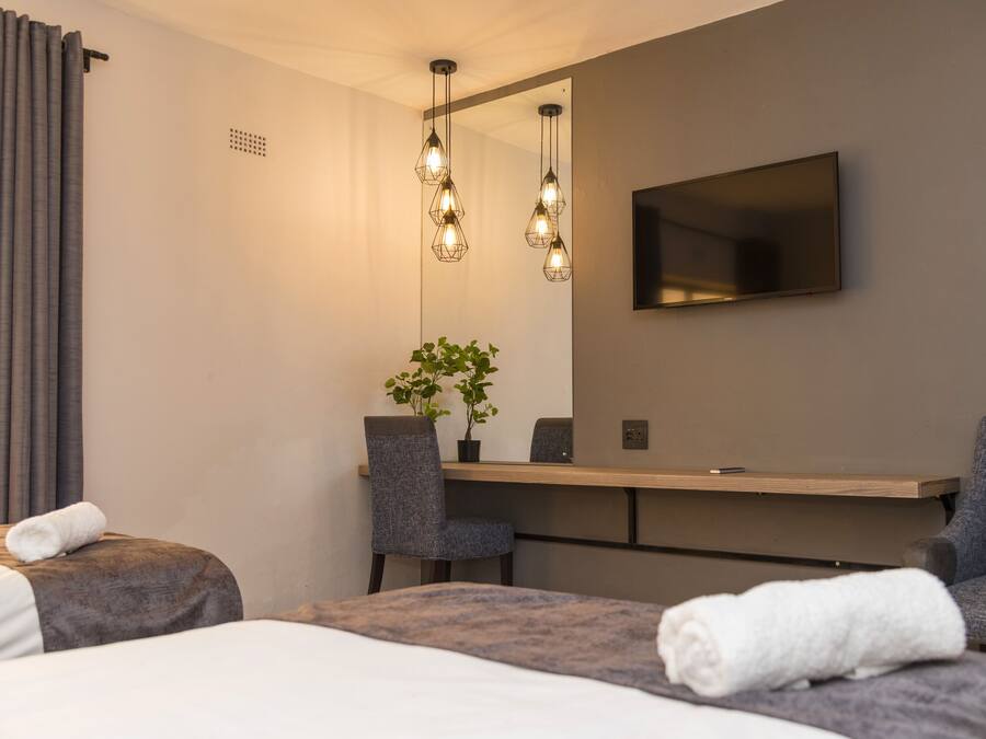 Una habitación de hotel moderna con cama, dos sillones, un escritorio, televisor de pantalla plana y lámparas colgantes.