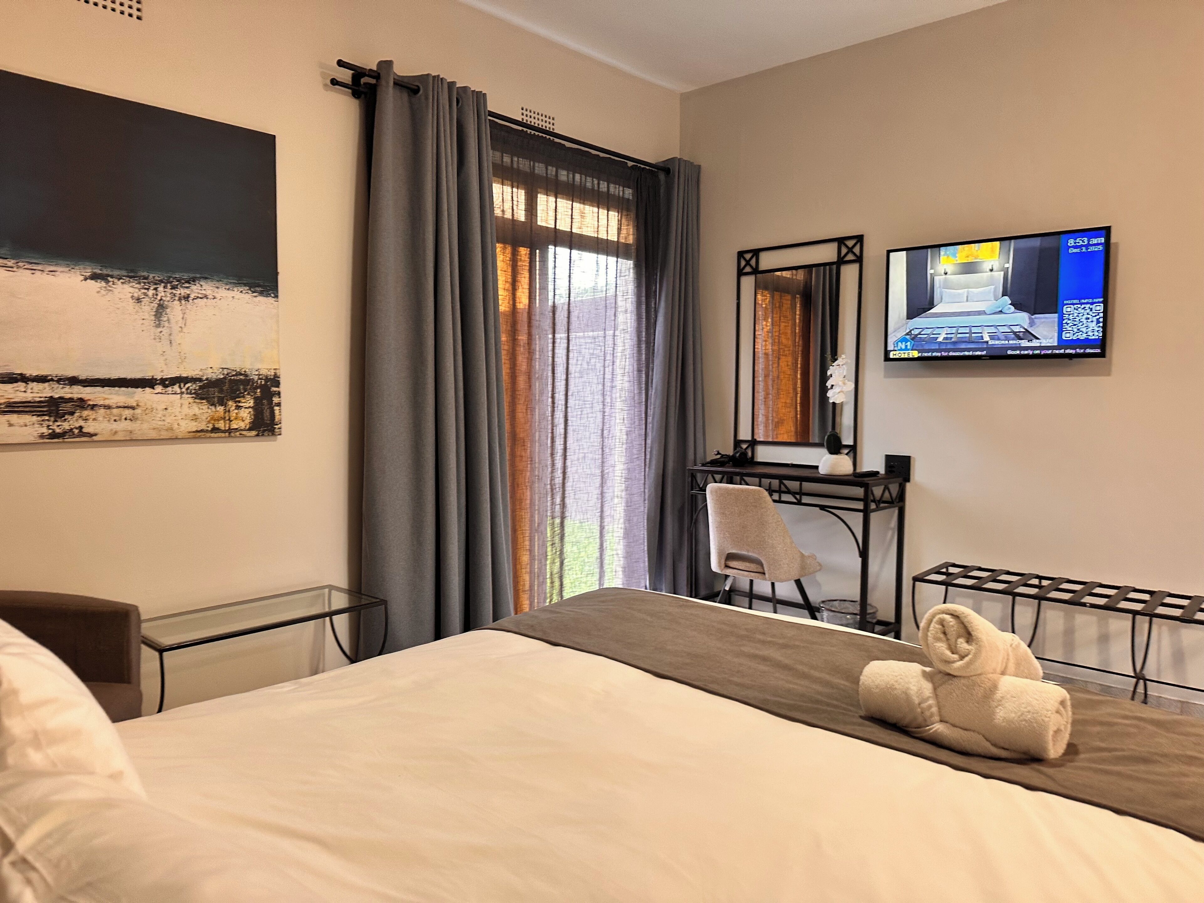 A hotel room with a bed, a desk, a chair, a TV, and a window with curtains.
