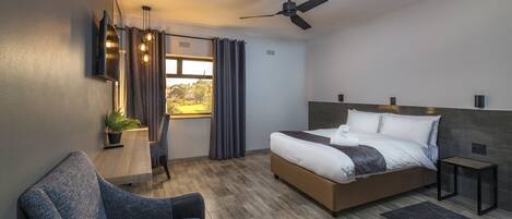 A modern hotel room with a large bed, a desk with a lamp, a chair, and a view of the outdoors.