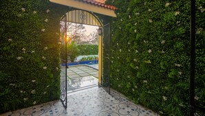 An open gate leading to a courtyard with a tiled floor and a view of a garden. - Justa Casa Frangipani Assagao, Goa (Assagao)