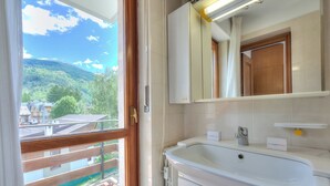 Une salle de bain dotée d’une grande fenêtre, d’un lavabo, d’un miroir et donnant sur un balcon avec une balustrade en bois.