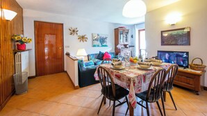Un coin repas avec une table dressée pour quatre personnes, un téléviseur posé sur un meuble en bois et un canapé avec des coussins en arrière-plan.