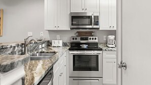 Una cucina moderna con mobili bianchi, un forno a microonde in acciaio inossidabile, un piano cottura a gas, una macchina da caffè e un ripiano in marmo.